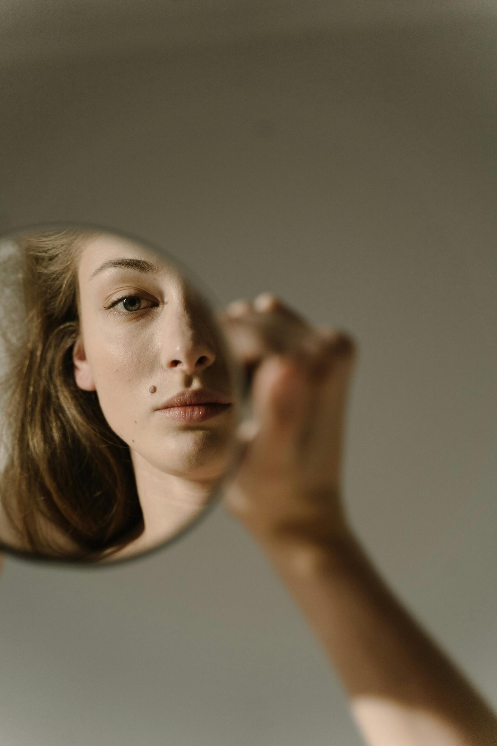 A woman holding a hand mirror that reflects her own face — a metaphor for AI mirroring back the way we think