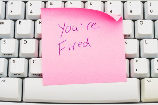 Pink sticky note on a keyboard reading You're Fired